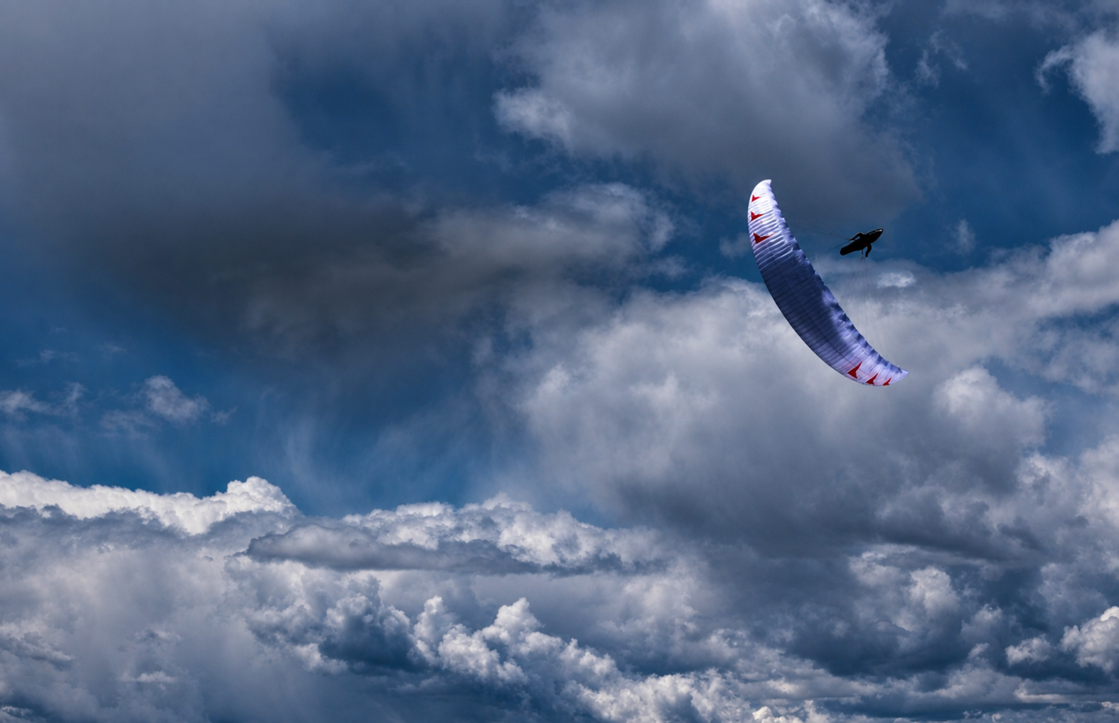 A paraglider flying beneath dramatic clouds
